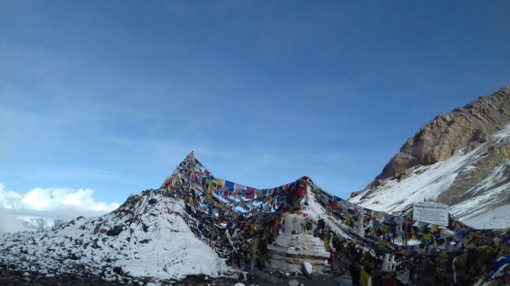 "Rugged terrain and sweeping mountain vistas at Thorong La Pass, the highest point on the Annapurna Circuit, covered with snow and marked with prayer flags fluttering in the cold, high-altitude wind."

